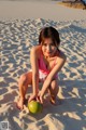 A woman in a pink bathing suit crouching down on a beach.