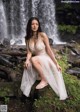 A woman in a white dress sitting in front of a waterfall.