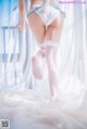 A woman in a white lingerie and stockings is standing on a bed.