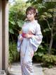 A woman in a blue and pink kimono standing in front of a building.