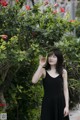 A woman in a black dress standing in front of a bush.