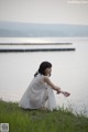 A woman in a white dress sitting on the grass by the water.