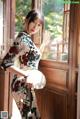 A woman in a cheongsam holding a fan in front of a window.