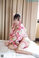 A woman in a pink kimono sitting on a bed.