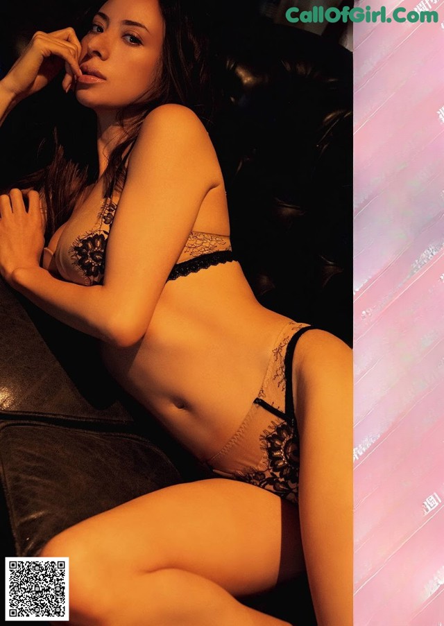 A woman in a black lingerie sitting on a couch.