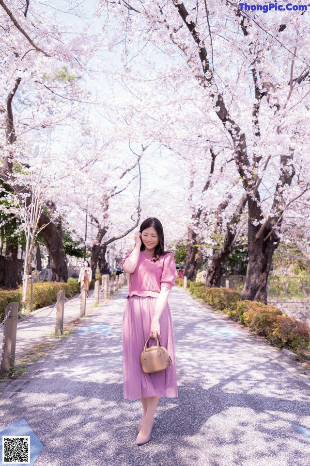 A woman in a pink dress is walking down a path with cherry blossoms.