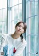 A woman sitting in front of a window wearing a white shirt.